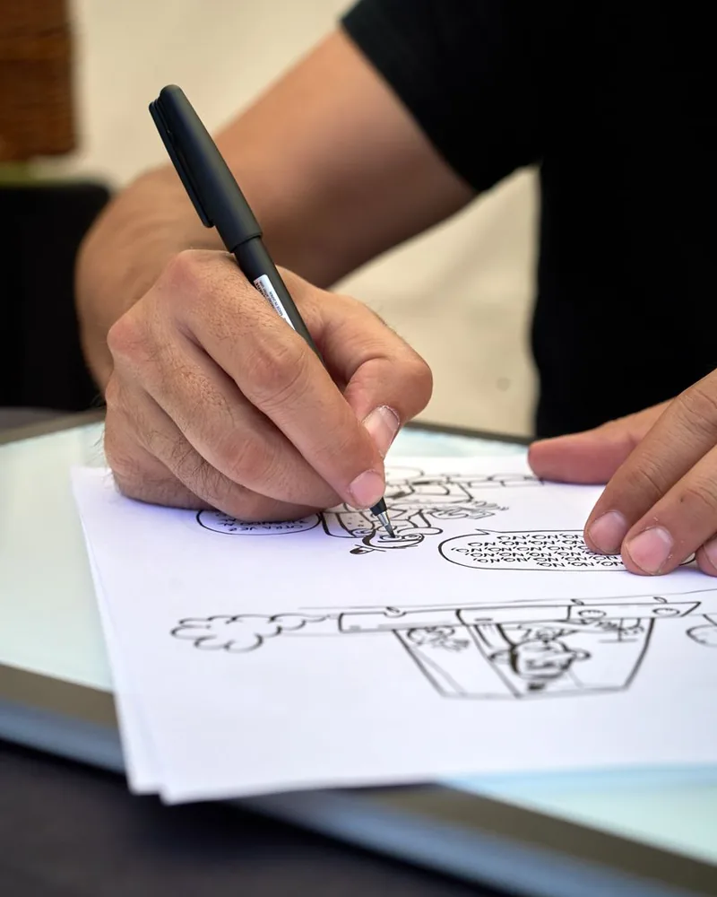 Manos entintando con rotulador unas viñetas de cómic dibujadas a lápiz sobre una mesa de luz
