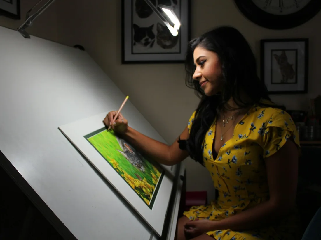 Persona dibujando sobre una mesa de dibujo inclinada iluminada por una lámpara articulada